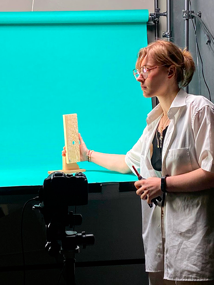 lisa_barozzi photo de Lisa BAROZZI en train de placer une planche de bois pour une photo d'une animation en stop motion, sur un fond en papier bleu
